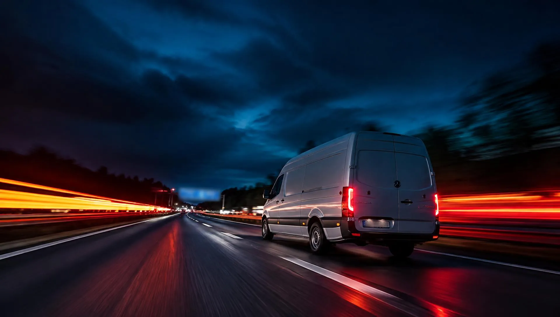 Weißer Transporter nachts auf der Autobahn, daneben Lichtspuren anderer Fahrzeuge